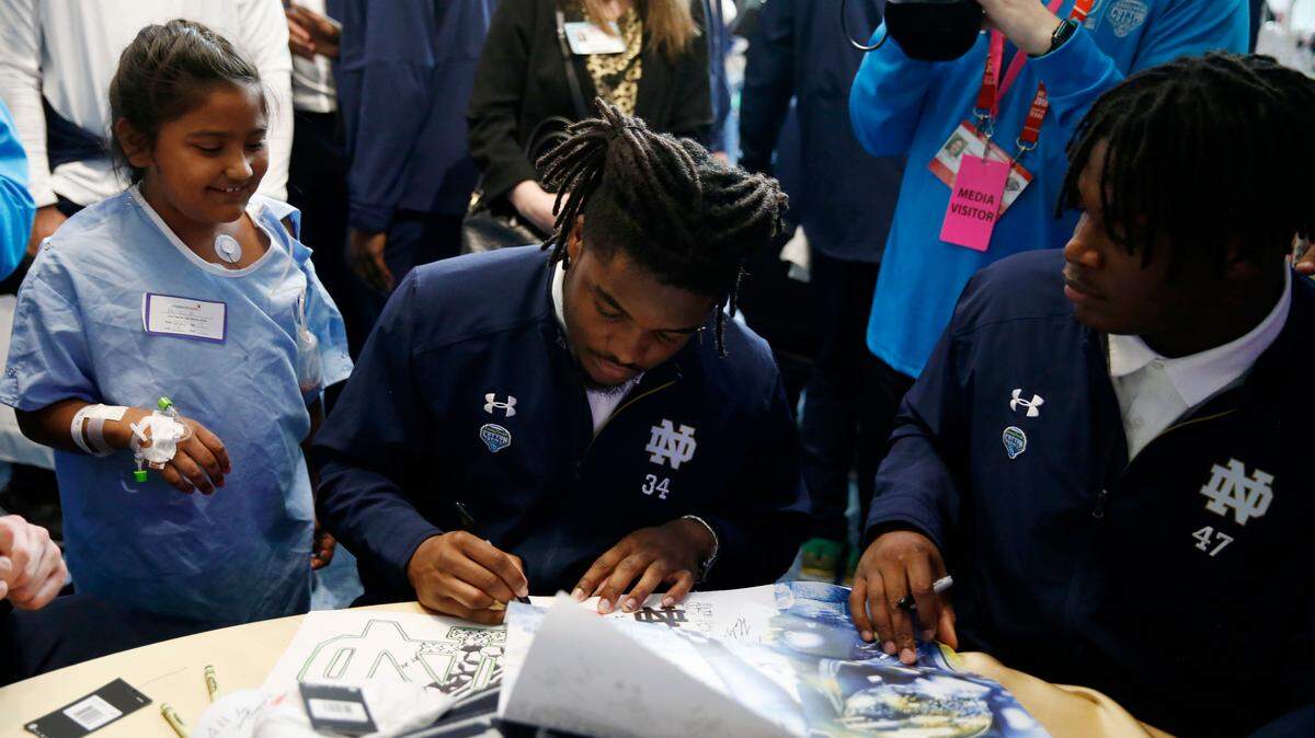 Anelle Aguero, 7, left, gets Notre Dame running back Jahmir Smith, center, to sign her poster as defensive lineman Kofi Wardlow watches during a hospital visit at Children’s Health in Dallas, Thursday, Dec. 27, 2018. Clemson will play Notre Dame at the Cotton Bowl on Saturday. (Vernon Bryan/The Dallas Morning News via AP)
