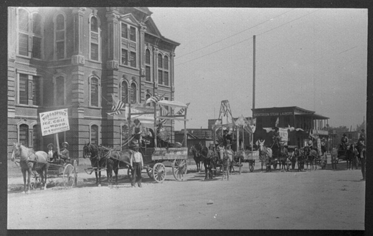 Circa 1897: Labor Day parade entry of Mugg & Dryden Ice, Coal and Wood Company, in front of county jail, Fort Worth, Texas. Mugg is in buggy (left) and Puckett is on right; Dryden in front of first dray driven by Leonard Zinn, boy in wagon is Earle Mugg.