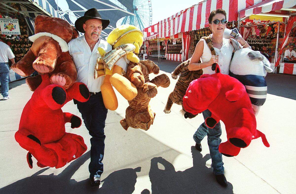 Sept. 29, 2000: Ron Lemley, left, is the Midway’s worst nightmare: a good eye, a love of the game challenge, and a pocketful of money snagged him and his wife Bobbie 11 of the biggest stuffed animals you could choose. The prizes were so big and so hard to carry, the Lemleys gave away two to passing children on the State Fair of Texas Midway. Last year they donated the 50 stuffed animals they won to charity. Here, the Dallas couple carry nine of the prizes back to their car. He threw softballs at milk jugs, pitched basketballs and footballs, any game on the Midway he tried and won, usually after only one try.