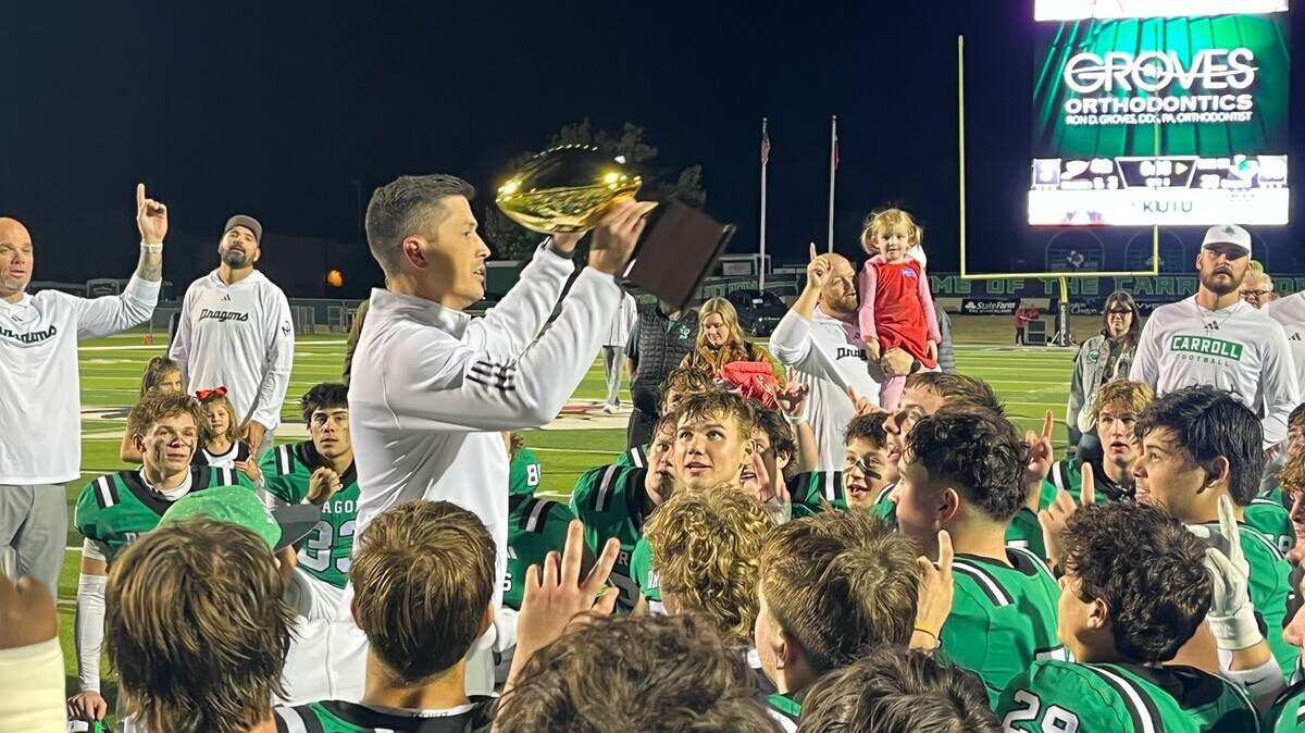 Southlake Carroll head coach Riley Dodge hoists the District 4-6A championship trophy Friday at Dragon Stadium in Southlake.