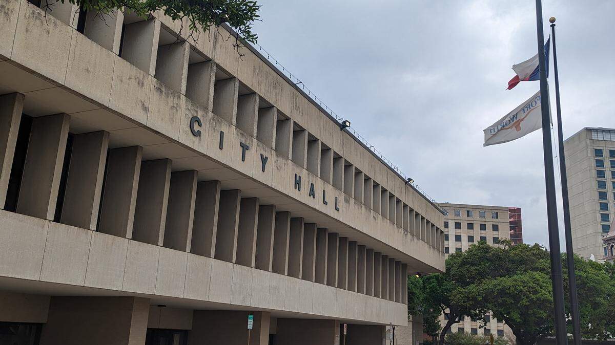 Fort Worth's concrete city hall building with an overcast sky and city of Fort Worth flag in the background. 