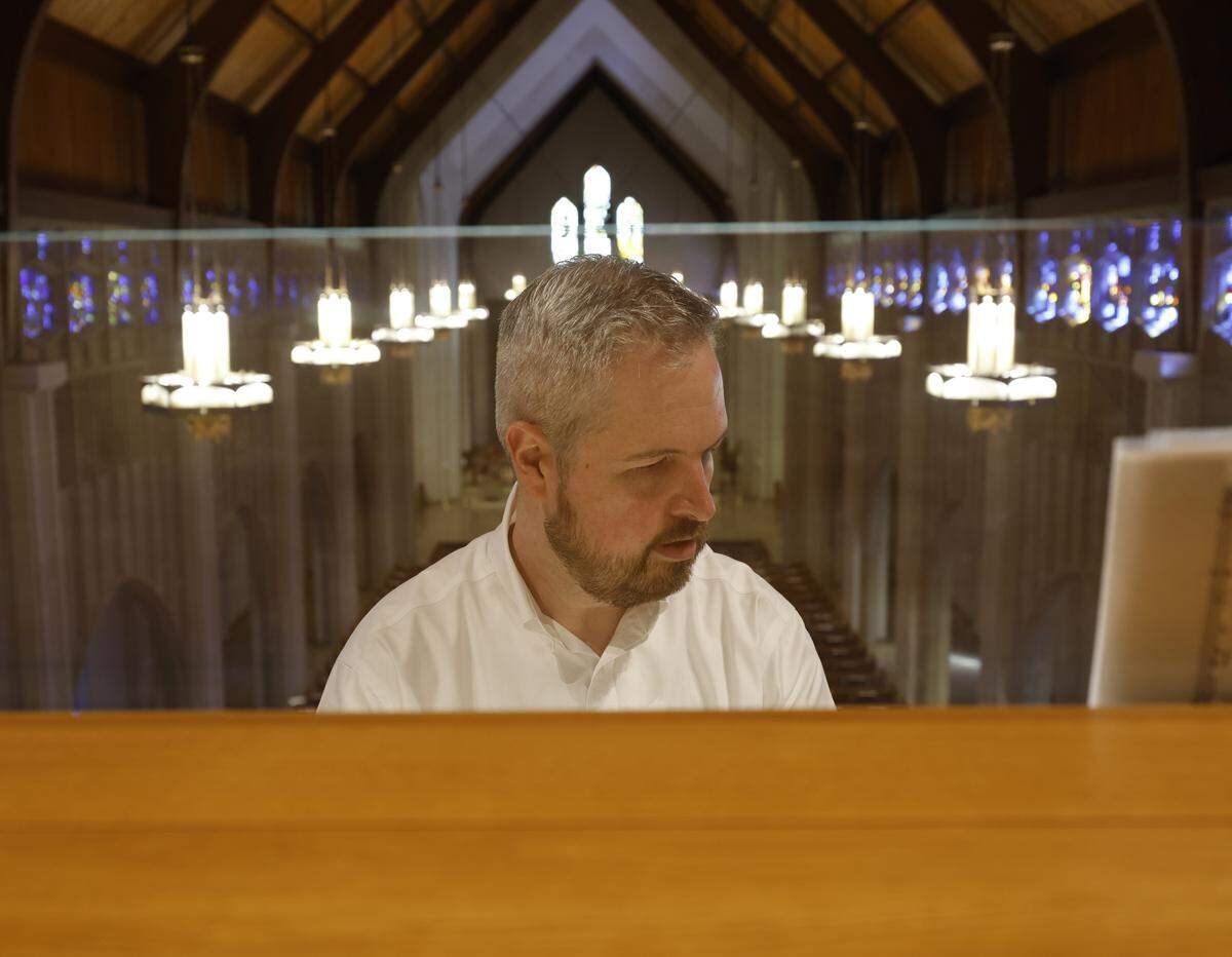 Organist Jordan Smith sits at the console of while the lights of the church glow behind him.