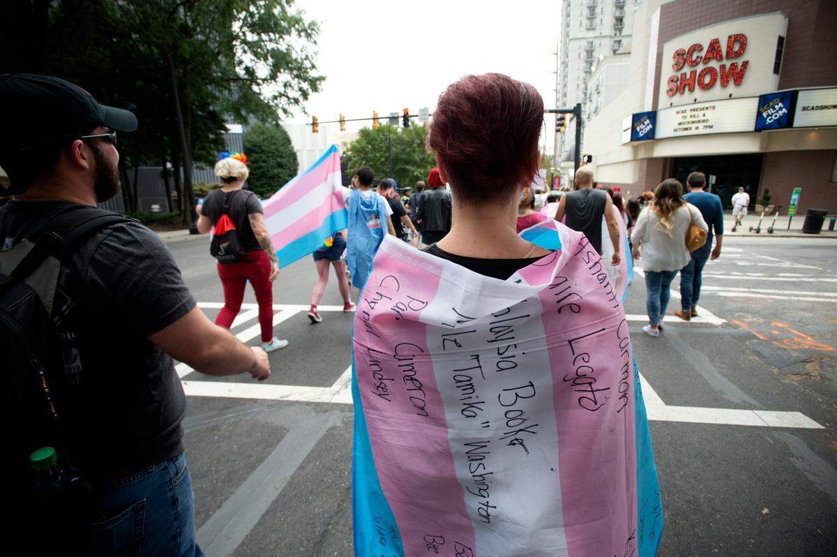 In this AP file photo from Oct. 12, 2019, A supporter for the transgender and non-binary community, wearing a transgender flag with handwritten names of black trans women who the person said were killed in 2019, strolls through the city’s Midtown district during Gay Pride Festival’s Transgender Rights March in Atlanta.