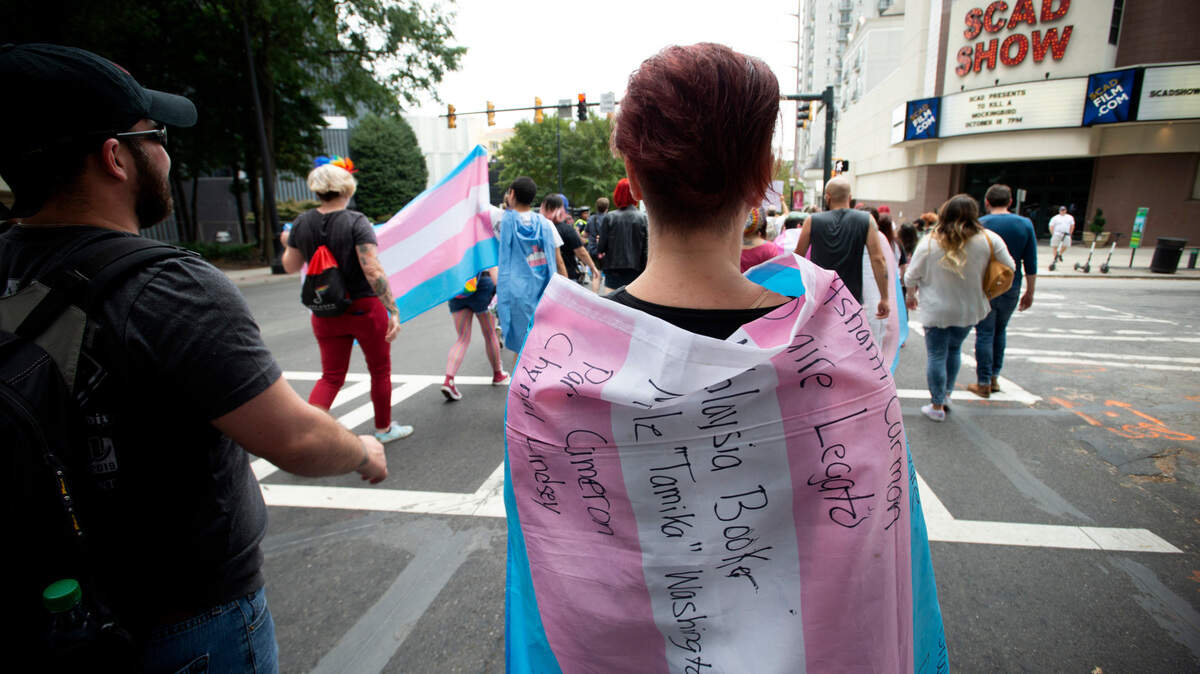 In this AP file photo from Oct. 12, 2019, A supporter for the transgender and non-binary community, wearing a transgender flag with handwritten names of black trans women who the person said were killed in 2019, strolls through the city’s Midtown district during Gay Pride Festival’s Transgender Rights March in Atlanta.