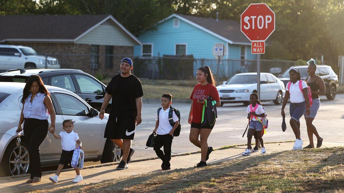 A man and a woman walk down a sidewalk with three kids.