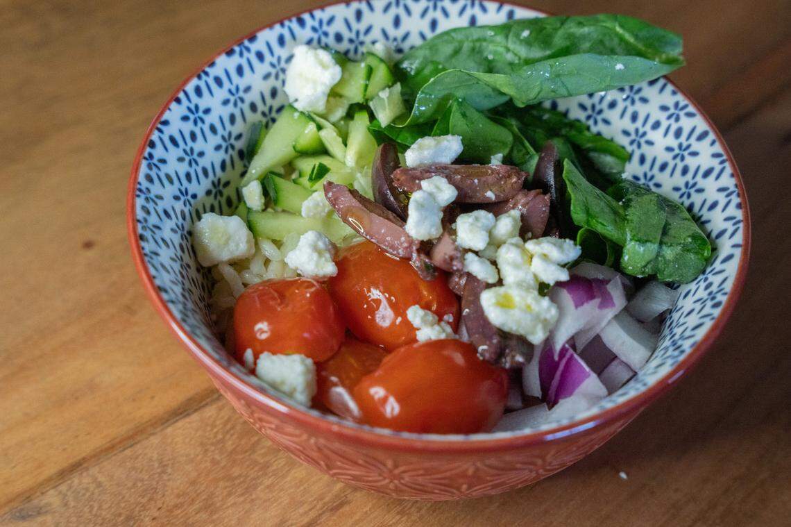 Mediterranean bowl at center, with fresh vegetables and olive oil on top.