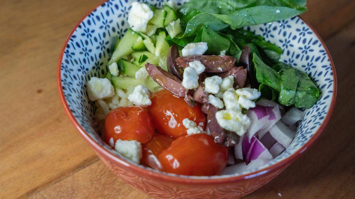 Mediterranean bowl at center, with fresh vegetables and olive oil on top.