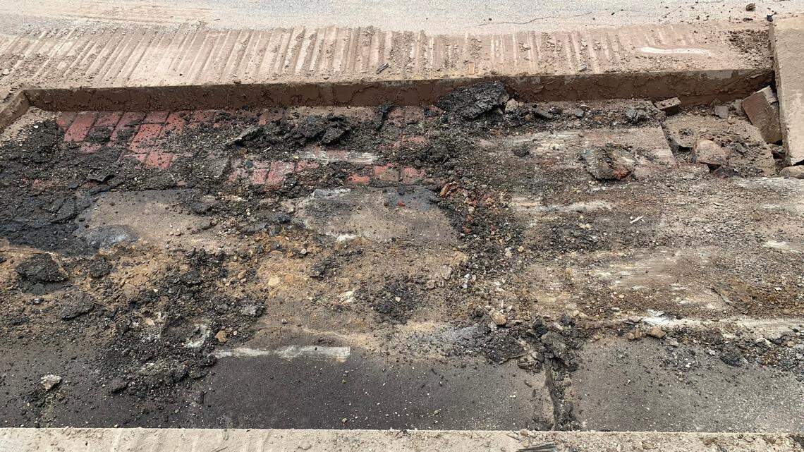 Red bricks poking out from under black asphalt a couple inches under existing roadway on West 7th Street in Fort Worth, Texas.