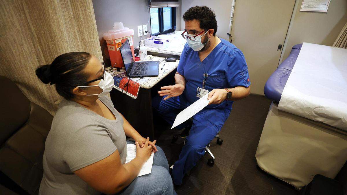 Nurse Pierre Claros, right, talks to Adriana Salcido-Macias before administrating the Pfizer vaccine in October at a Texas Health Resources mobile clinic.