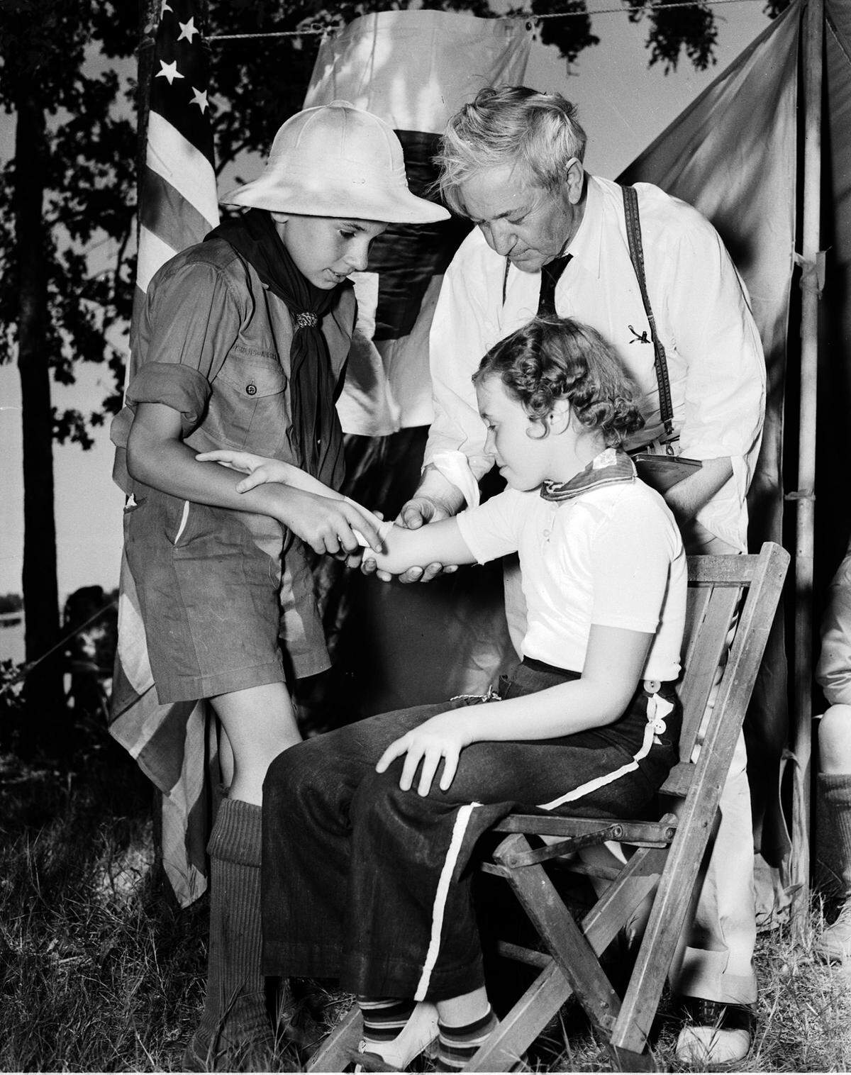 July 4, 1938: Catholics celebrate 4th of July with picnic at Lake Worth; Charles Edward Breen in Boy Scout uniform bandages a scratch on his sister’s arm (Patsy) while supervised by Dr. M.V. Creagan.