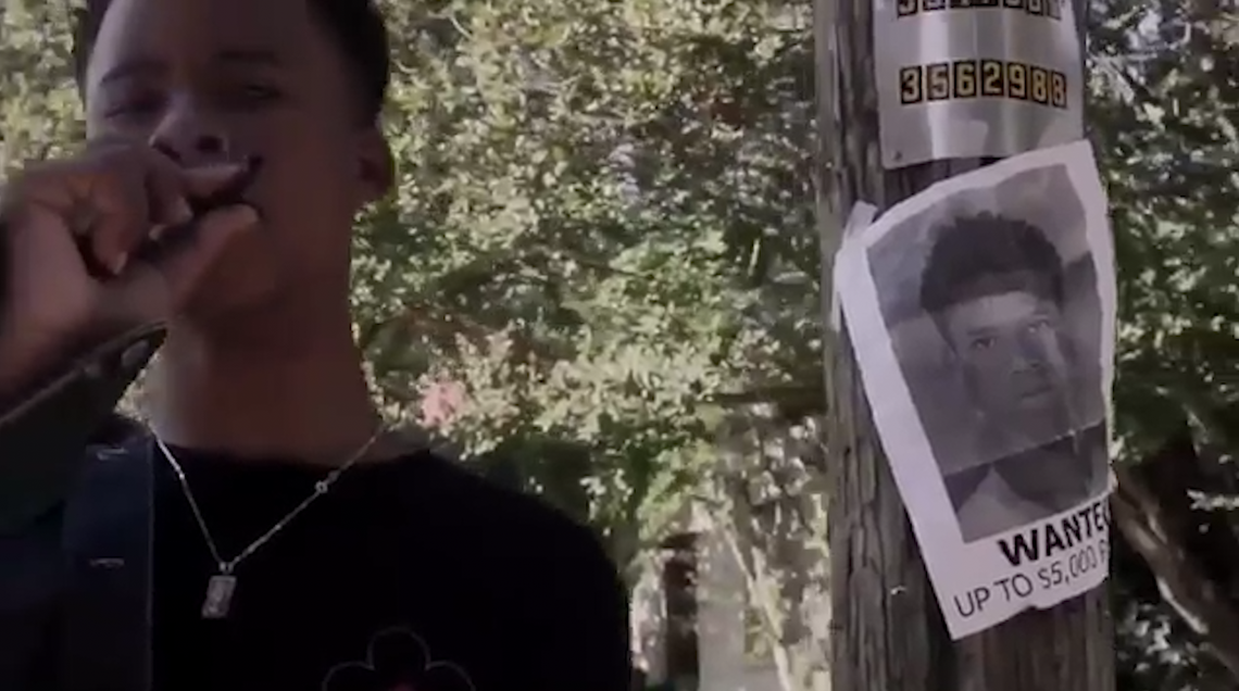A screen shot of Taymor “Tay-K 47” McIntyre, taken from a video released on YouTube, shows the rapper posing in front of a wanted poster of himself.