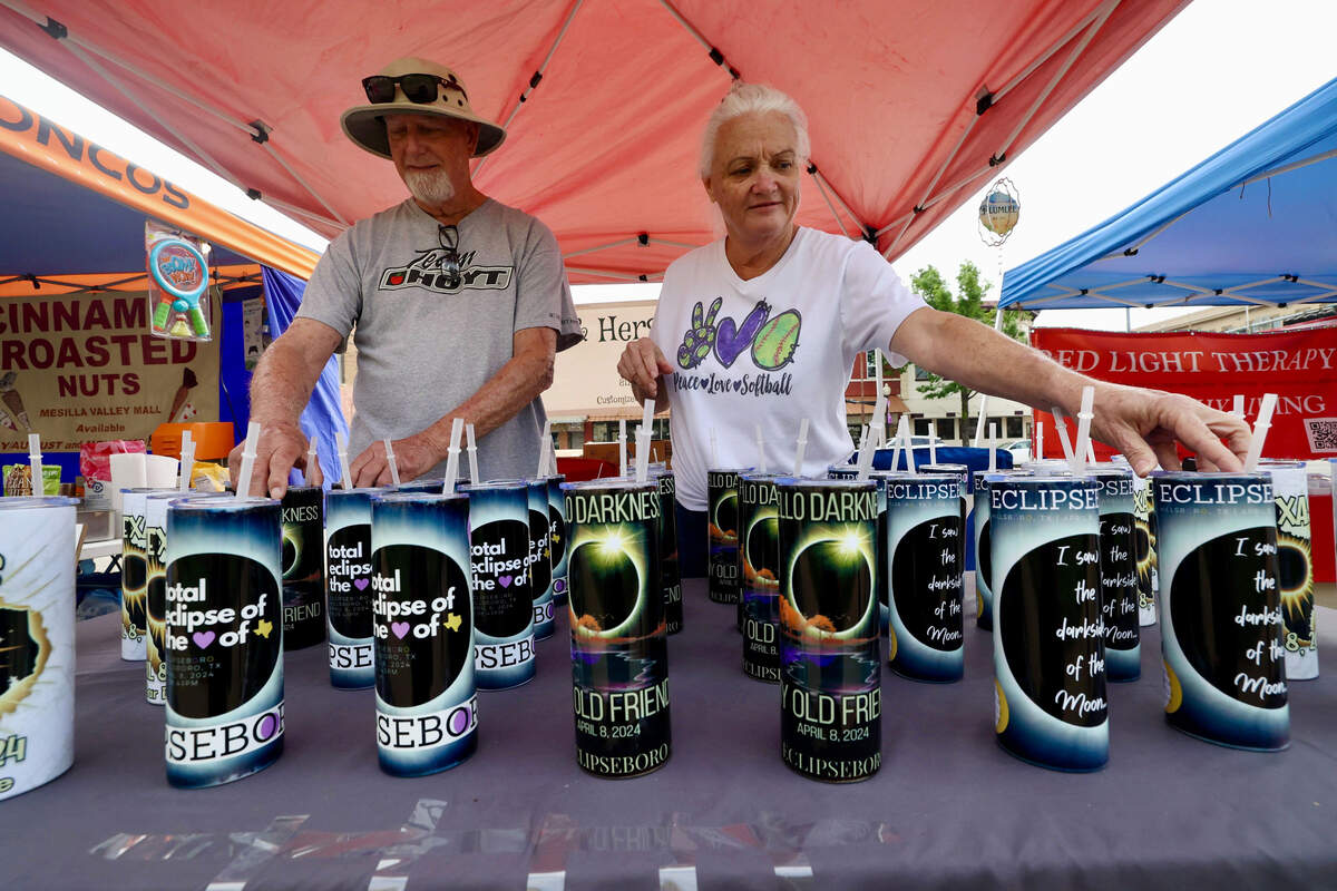 A man and woman line up tumblers with straws under a red tent. 