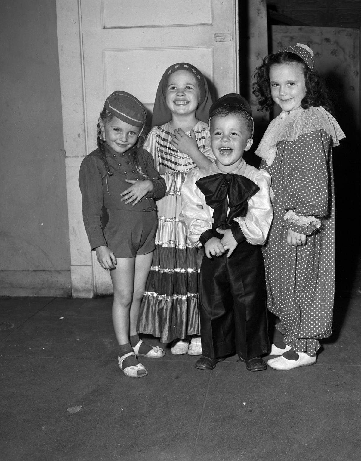 The group of four are shown together as they smile and laugh at the camera with each of them wearing a different costume including Judy Chambers wearing a clown costume and Judy Nickerson wearing a bellhop costume. 