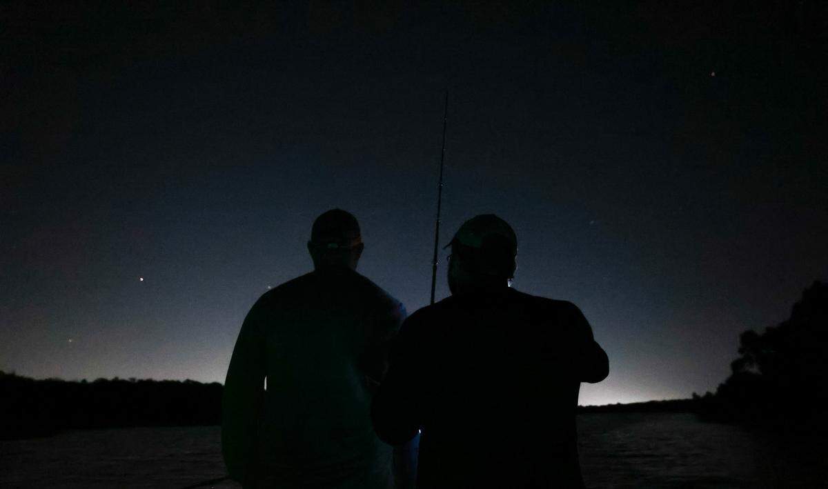 Two men holding fishing poles are silhouetted against a dark night sky.