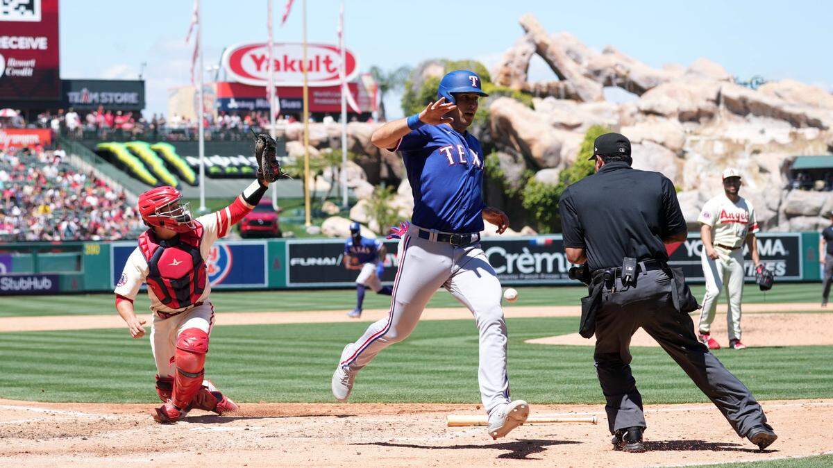 Texas Rangers first baseman Nathaniel Lowe (30) beats a throw to Los Angeles Angels catcher Matt Thaiss (21) to score in the fourth inning as home plate umpire Nestor Ceja watches at Angel Stadium.