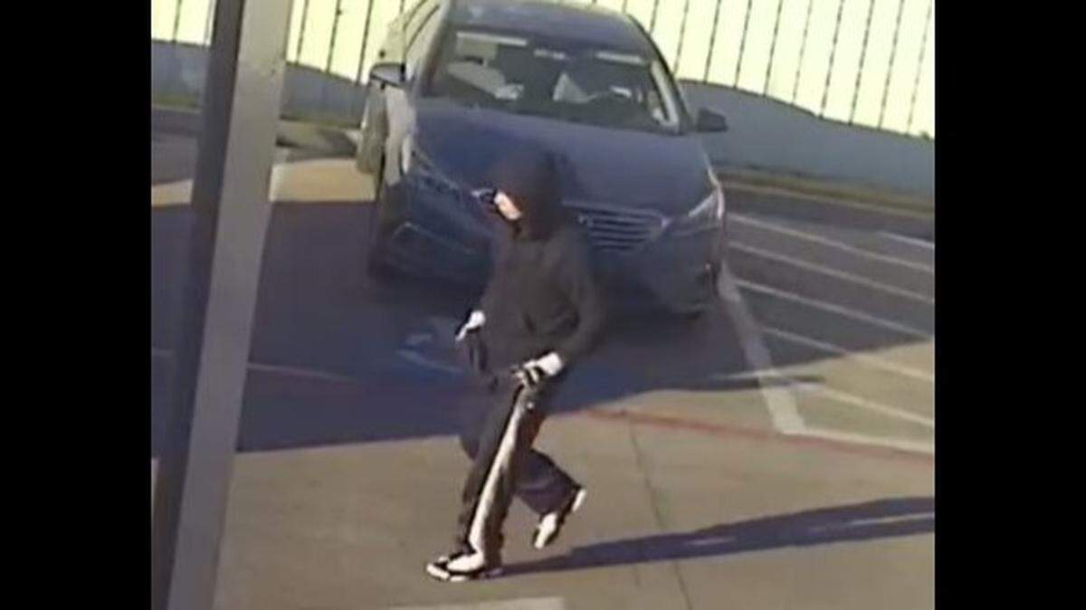 Surveillance photos show the man wearing a black hoodie, black joggers with a white stripe down the sides, black and white shoes, and a red face mask.&nbsp;