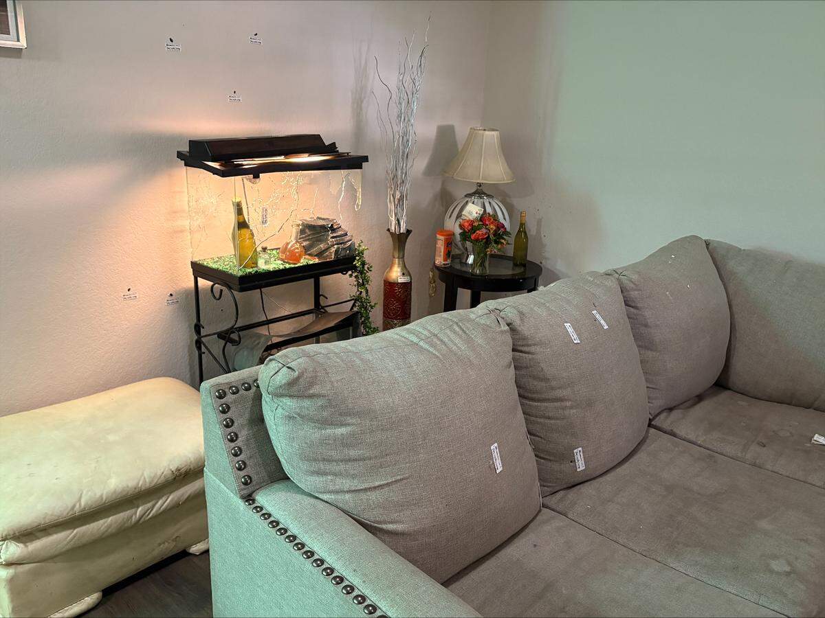 A couch and fish tank in James Washington’s Fort Worth home are riddled with bullet holes and police markers after a drive-by shooting at the house early on April 2, 2026.