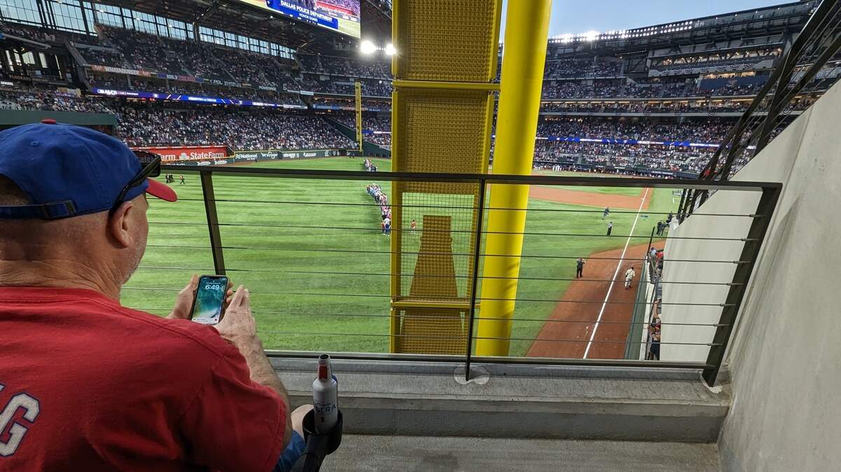A man sits behind a foul pole at a baseball stadium blocking his view of the field. 