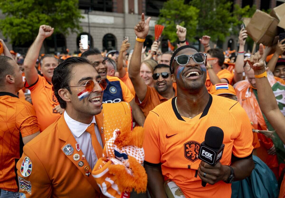 New York Giants quarterback Jameis Winston and Daniel Oordt, the “Oranje Suit Man” dance with other fans ahead of the orange fan walk on Sunday, June 14, 2026 in Arlington, Texas. The famous double-decker Dutch Orange Bus, or De beroemde Oranjebus, is part of a Netherlands fan tradition bringing a sea of orange to the streets before major soccer matches.