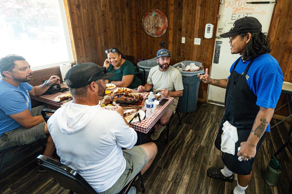 Nupohn Inthanousay, one of the co-owners of Goldee’s Barbecue, speaks with Chris Dupree, Matt Mueller, Jeff McDonald, and Lindsay Dupree as they eat their tray of barbecue in the Goldee’s dining room at Fort Worth on Friday, June 28, 2024.