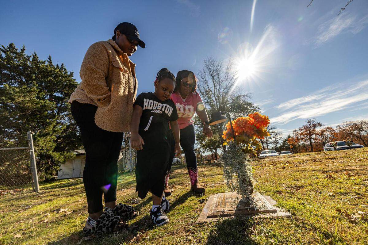 LaKeisha Mackey, middle, prays with her daughter Dererica Johnson, left, and her granddaughter Kenzlee Carson, 5, at her son Derrick Johnson’s gravesite at Cedar Hill Memorial Park in Arlington on Sunday, Dec. 10, 2023. Mackey’s son Derrick was killed in a shooting in 2020 at 19 years of age. Along with her son, she also lost her father in 1989, her uncle in 1980 and her sister in 2017 to gun violence.