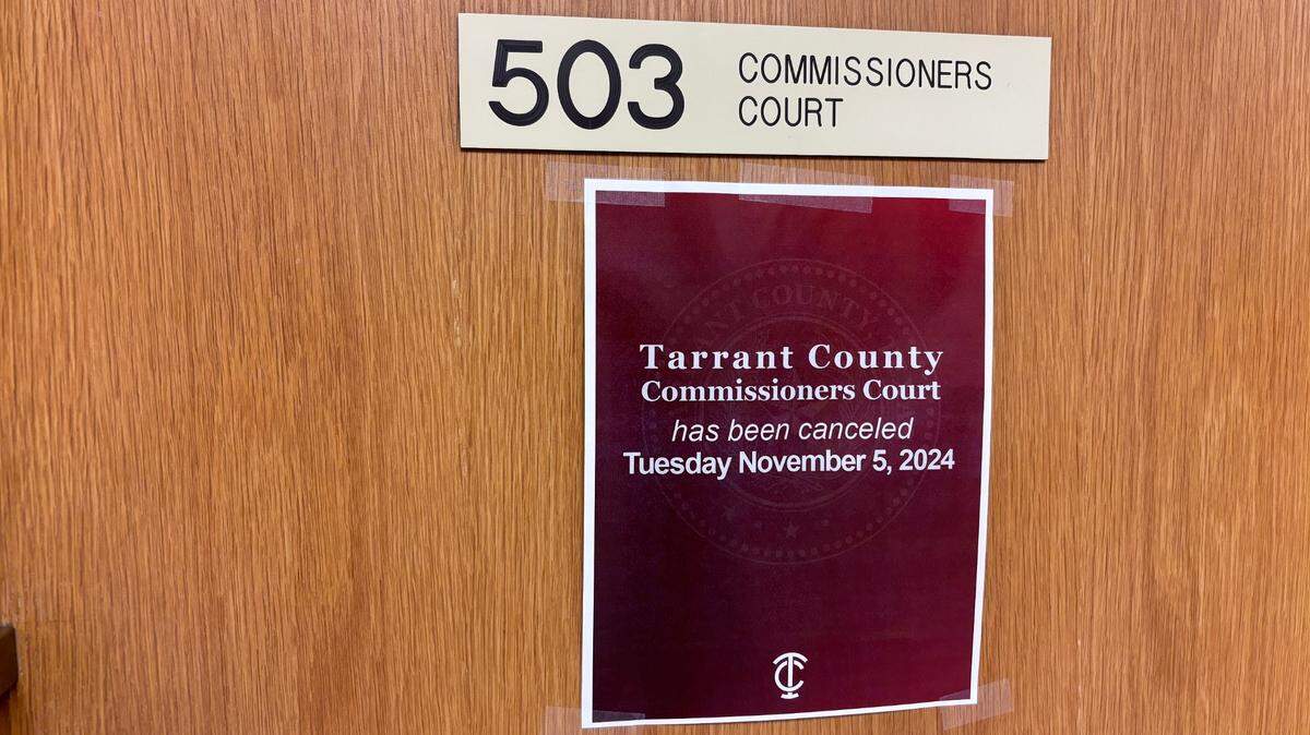 A paper sign posted on a wooden door has white text on a red background. A placard above the printed sheet reads '530 Commissioners Court'.
