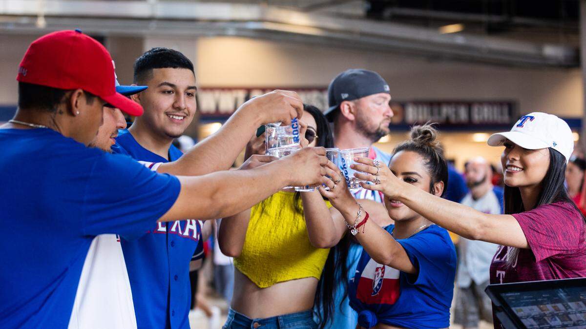 Friends cheer each other before doing shots from a concession stand during the Texas Rangers opening day game Monday, April 11, 2022, at Globe Life Field in Arlington.