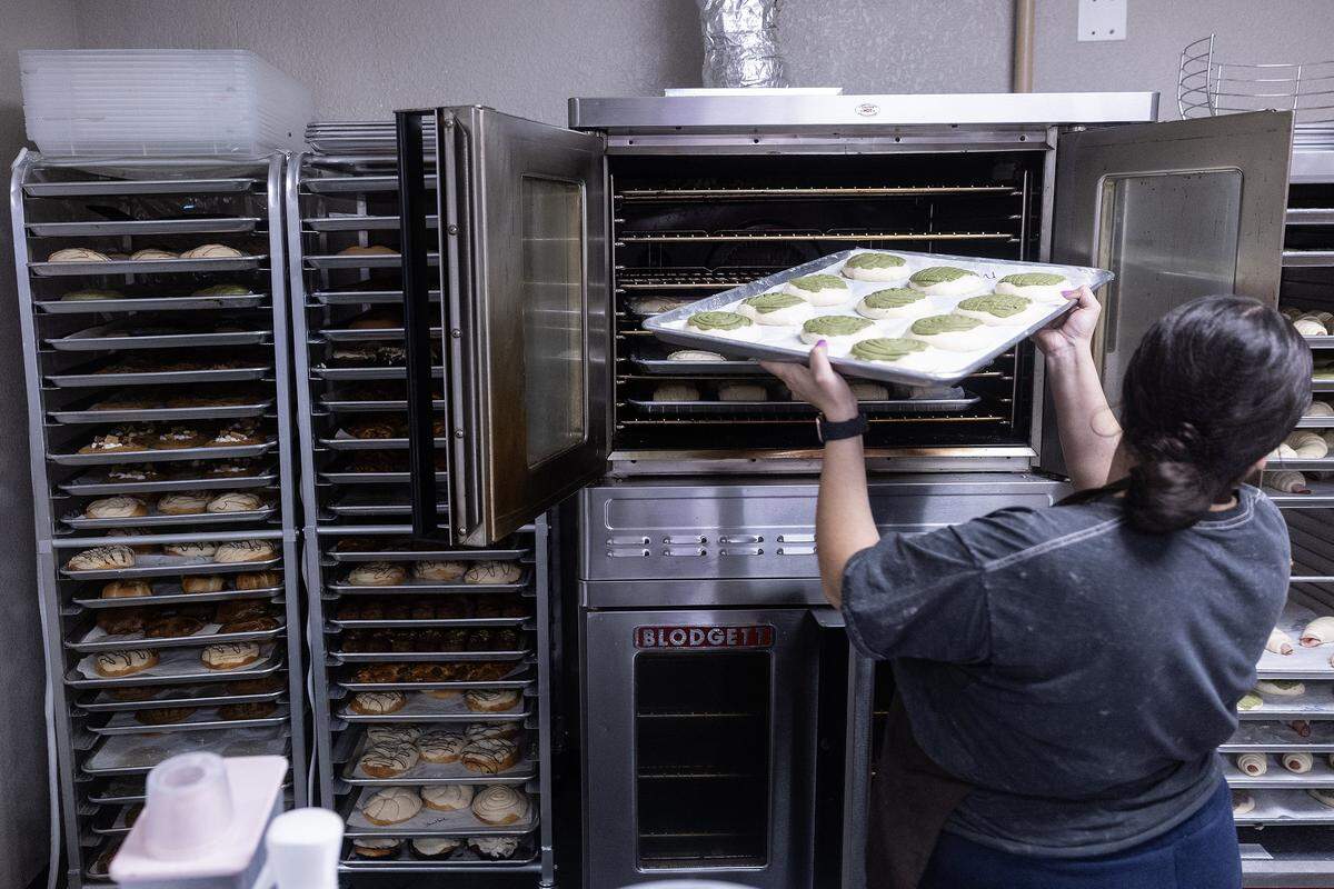 The head baker and back of house manager puts matcha conchas into the oven.