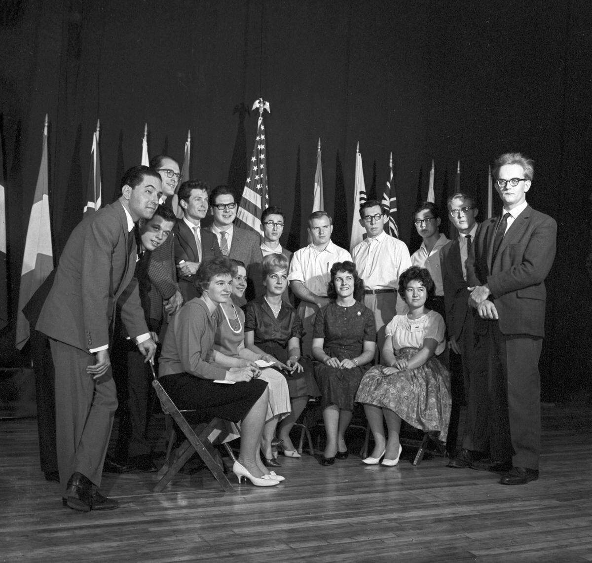 The 16 pianists selected to enter the final week of the competition in 1962, gathered in front of flags of the nations which they represented. Seated from left: Ilze Graubin and Nina Lelchuk of Russia, Cecile Ousset of France, Marilyn Neeley of California, and Hiroko Nakamura of Japan. Standing, from left: Sergio Varella-Cid of London, who was representing Portugal, Arthur Charles Fennimore of Pennsylvania, Donn-Alexandre Feder of New York, Mikhail Voskresenski and Nikolai Petrov of Russia, Hajime Kono of Japan, John Perry of Kansas, Raul Sosa of Argentina, and Takashi Andrew De Groote of Belgium.