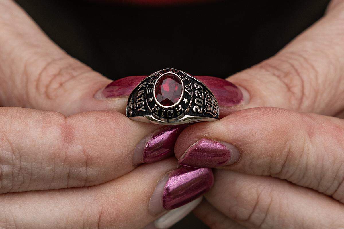 A tight shot of fingers with magenta painted nails holding a class ring with a red stone.