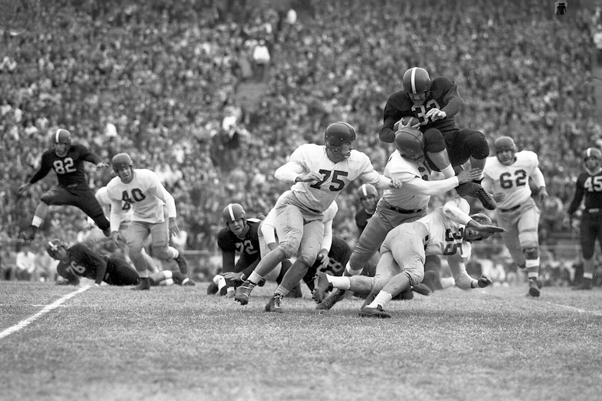 Bobby Jack Floyd, the Frogs’ jumping fullback, prepares for a crash landing as Neal Franklin (61) of Southern Methodist University (SMU) grasps his legs in 1950.