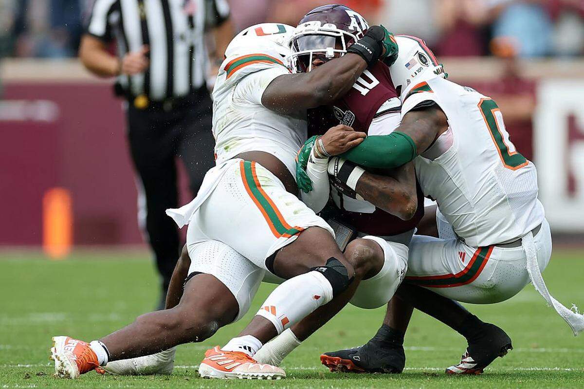COLLEGE STATION, TEXAS - DECEMBER 20: Marcel Reed #10 of the Texas A&M Aggies runs with the ball while being tackled by Mohamed Toure #1 and Keionte Scott #0 of the Miami Hurricanes in the first quarter during the 2025 College Football Playoff First Round Game at Kyle Field on December 20, 2025 in College Station, Texas. (Photo by Tim Warner/Getty Images)