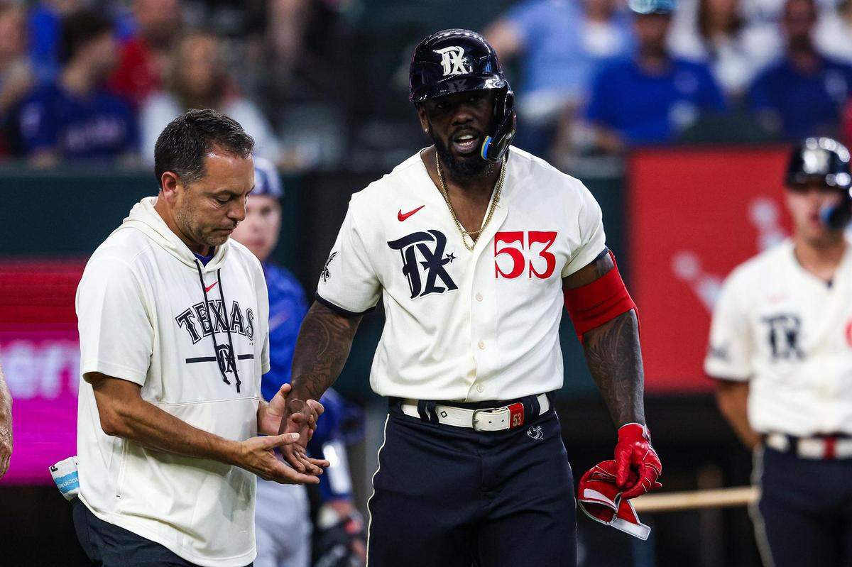 A Texas Rangers training staff member checks on outfielder Adolis Garcia (53) after getting hit in the hand by a pitch in the seventh inning of a regular season match up against the Los Angeles Dodgers at Globe Life Field in Arlington, Texas on Saturday, July 22, 2023. The Rangers gave up 18 hits and lost 16-3.