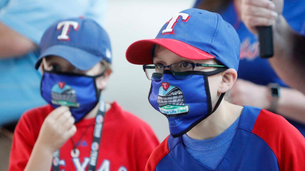 FILE - In this June 1, 2020, file photo, Gavin Bollmer, left, and his buddy, Austin LaFountain, wear Globe Life Field masks as they tour the home of the Texas Rangers baseball team in Arlington, Texas. Many organizations are trying to bridge the budget gap from the coronovirus through enhanced sponsorship sales, such as temporary billboards that could be stretched over unsold sections of seats. Teams and leagues are selling branded face masks and other personal protective equipment. Almost all of them are trying to engage fans in new and creative ways. It won’t come close to making up the budget shortfall, but the hope is to survive long enough for sports to return to normal. (AP Photo/LM Otero, File)