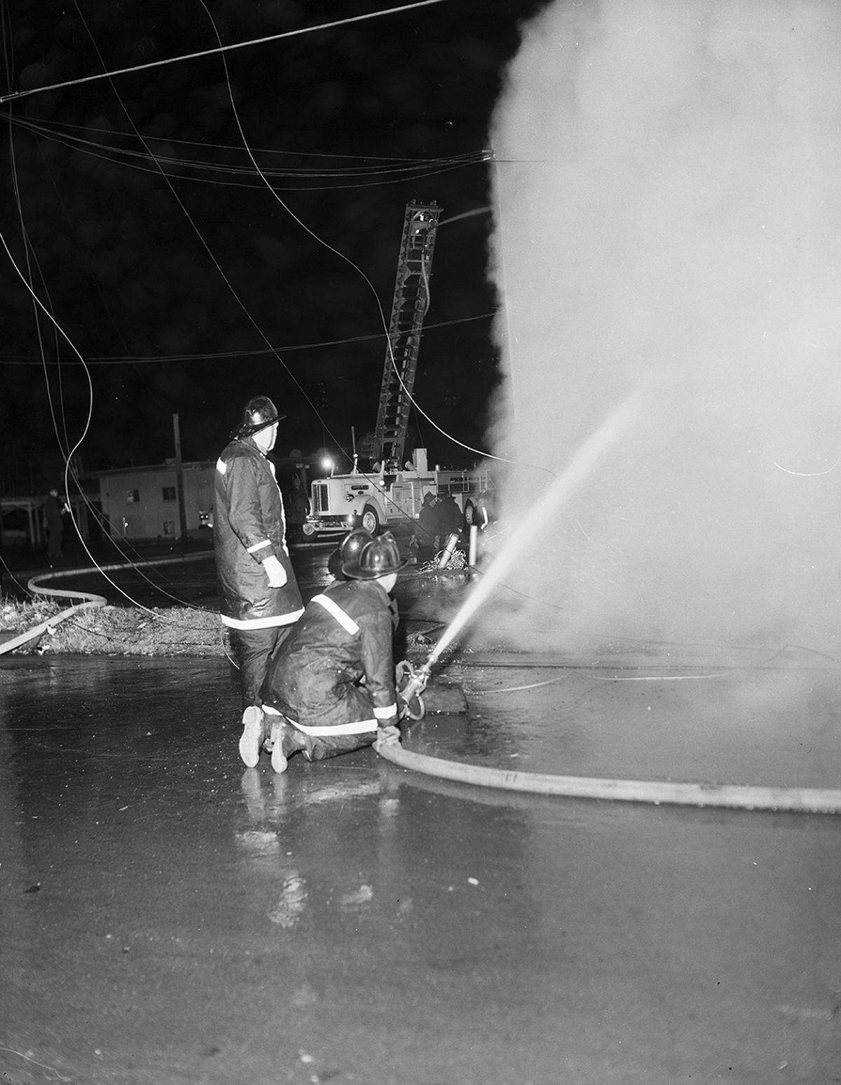 Feb. 2, 1959: Firemen kneel and crouch to direct a stream of water on smoke-covered wall of Buddies No. 12, 1503 North Main St., while a hose at top of ladder gives aerial support to attack. Wires sag around the firemen. (The site, 1503 N. Main St. at N.W. 14th Street, is home today a convenience store and laundry shop. In 1941, a Lovelace Grocery and Market at the same site also burned.)
