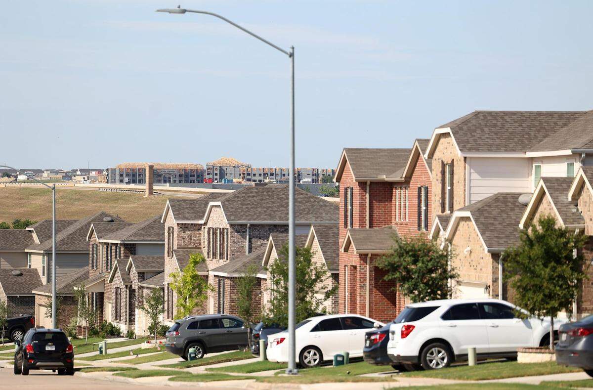 A road in a suburban subdivision with cars parked out front.  