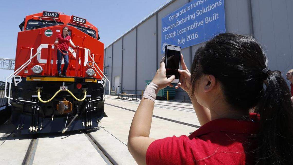 Employee Uyen Pham (right, cq) takes a photo of Lauren Judge posing in front of a shiny new locomotive at the General Electric Manufacturing Solutions Locomotive plant in Fort Worth in 2016.