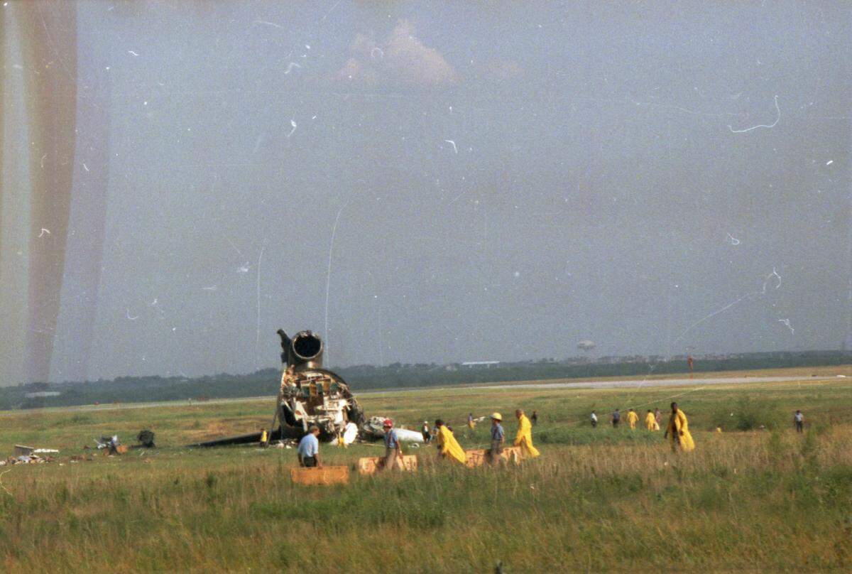  A color photo taken from a distance that shows people swarming the wreckage of the plane in a field.
