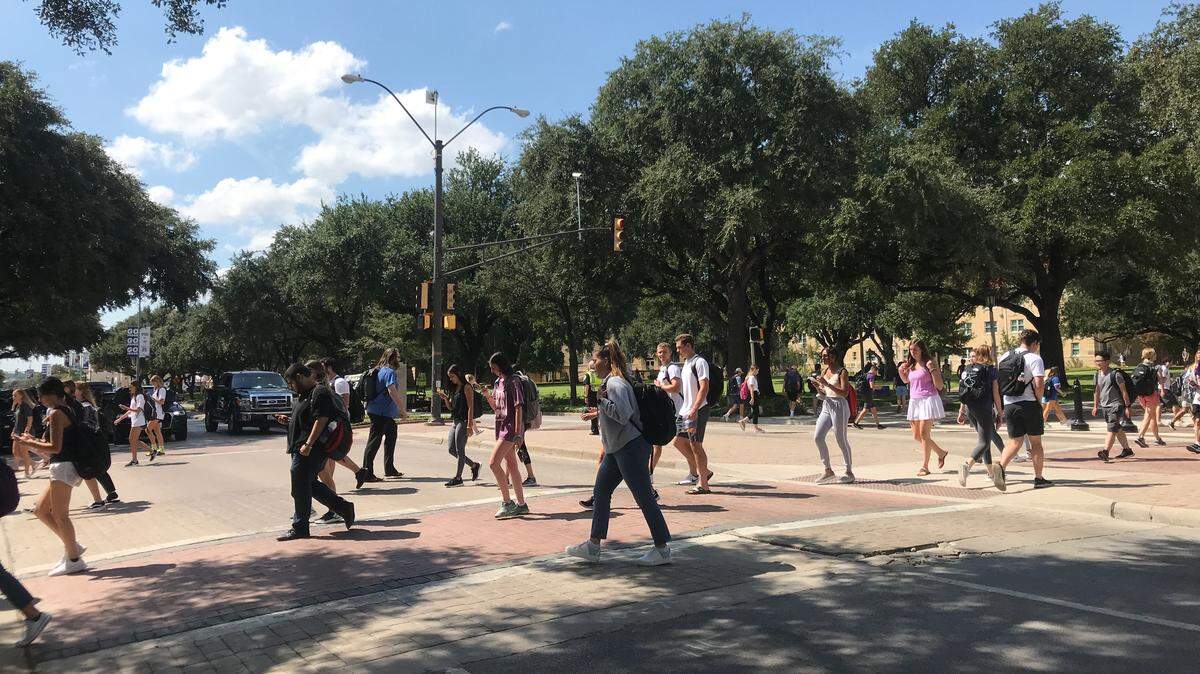 College students crossing a large tree lined street.
