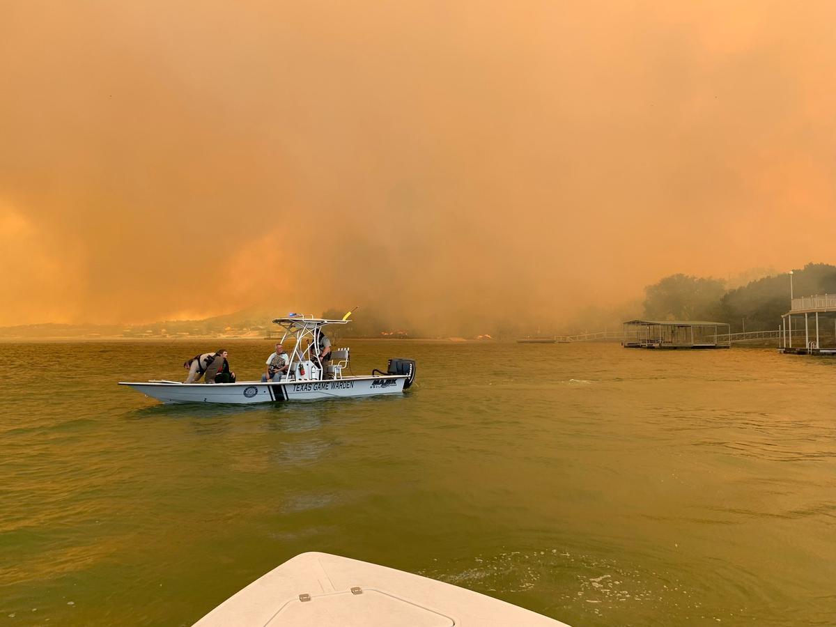 A game warden boat with four people floats on a lake in Palo Pinto County. The smoke filled sky in the background is orange from the wildfires.