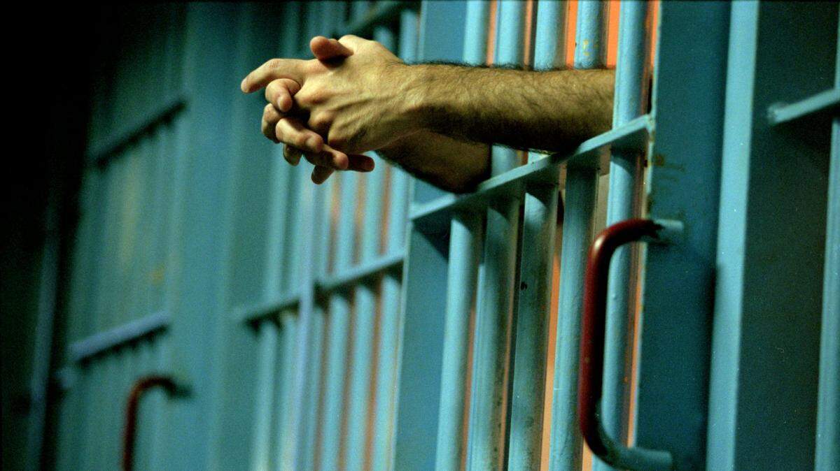 A photo of an inmate's hands through prison bars.