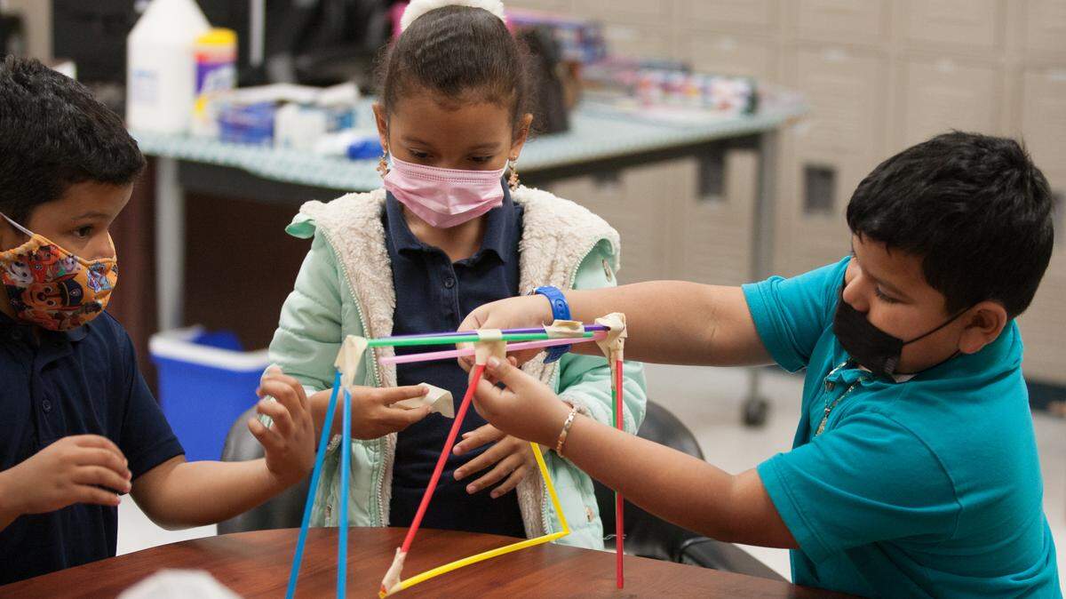 Three kids build a structure out of a STEM-based building set.
