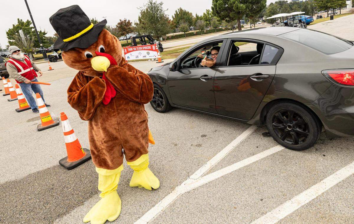 The Turkey mascot waves goodbye to people after picking up their groceries during the 4th annual Thanksgiving Mobile food distribution at AT&T Stadium in Arlington on Friday, November 17, 2023.