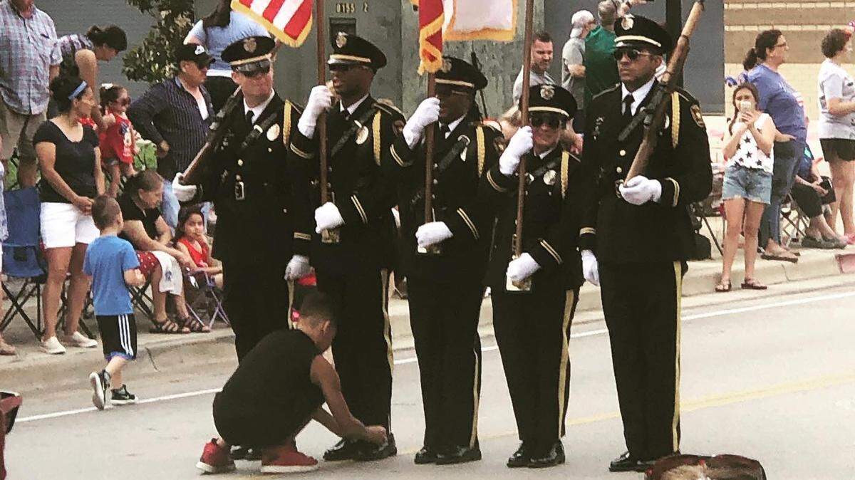 Joshua Brown kneels to tie the shoelace of Arlington police officer Jerrick Wilson during the July 4th parade. The photo became a viral sensation around the world.