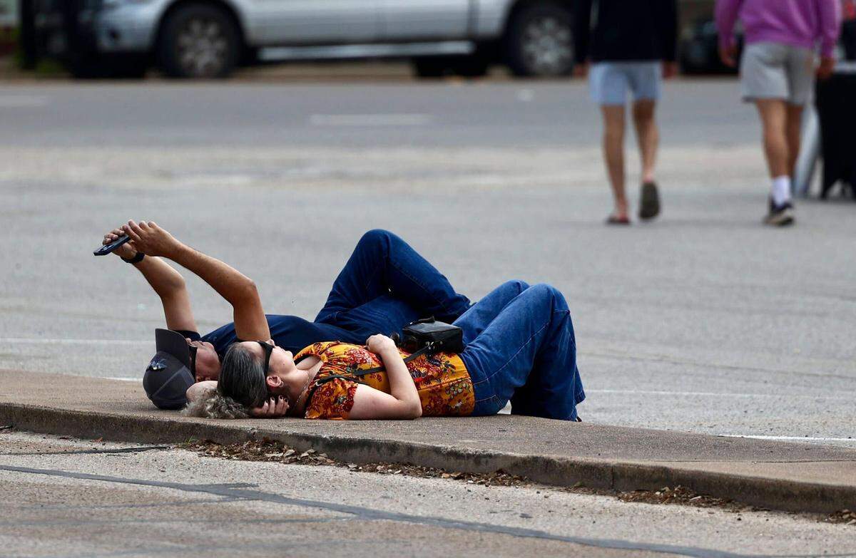 Hector Lopez and Margarita Velasquez from Houston attempt to use a phone to capture the eclipse while laying down on the street in Hillsboro.
