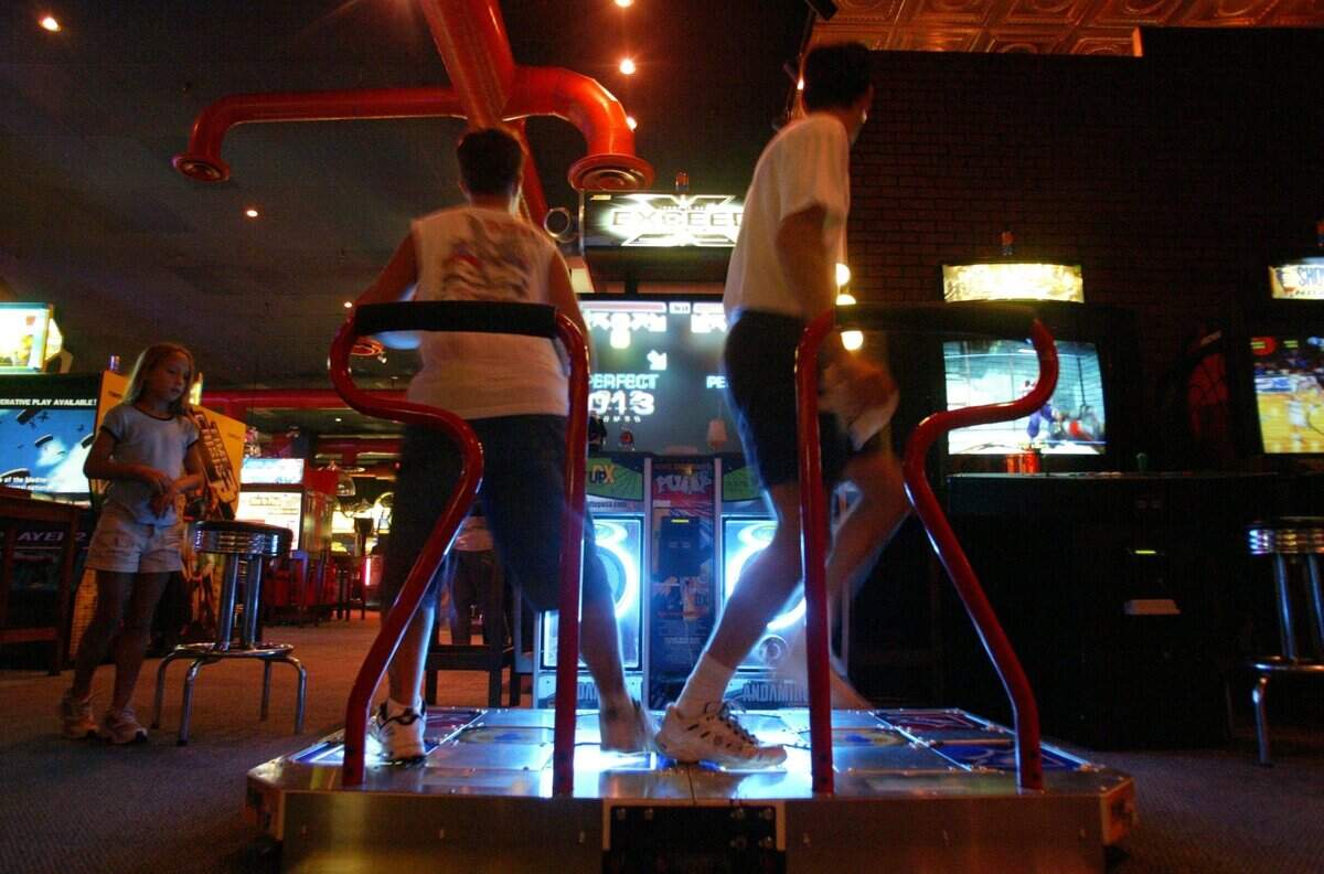 John Cook (left), 12, of Coppell, Texas, and Art Noxon, 43, of Dallas, Texas, play Pump It Up Exceed, a video dance machine, at Dave & Buster’s in Dallas on Saturday, July 24, 2004.