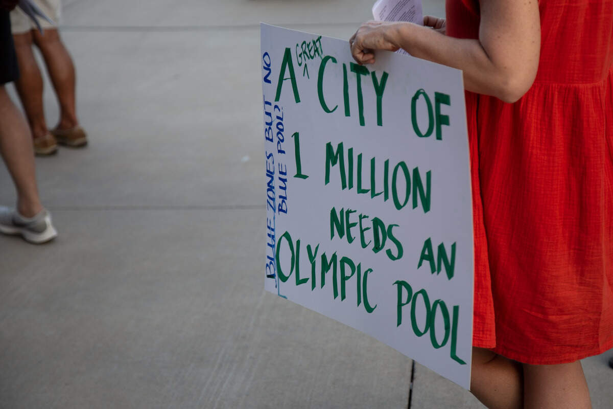 A woman holds up a sign at a community meeting to discuss replacing the Forest Park Pool.