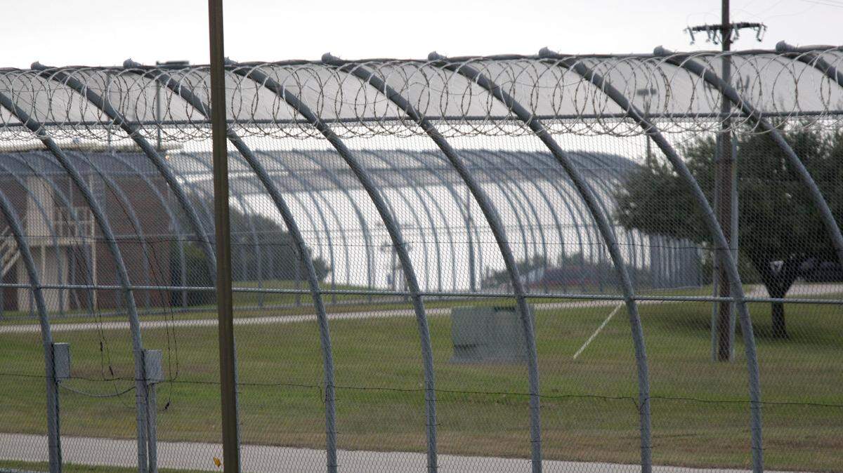 This archive photo shows the tall curved chain link fence topped with razor wire at the Gainesville State School.