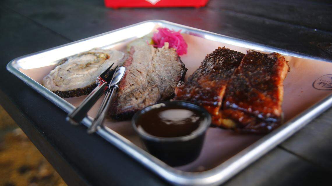 A trey of barbecue including ribs, Texas Porchetta, and beef sits on a table.