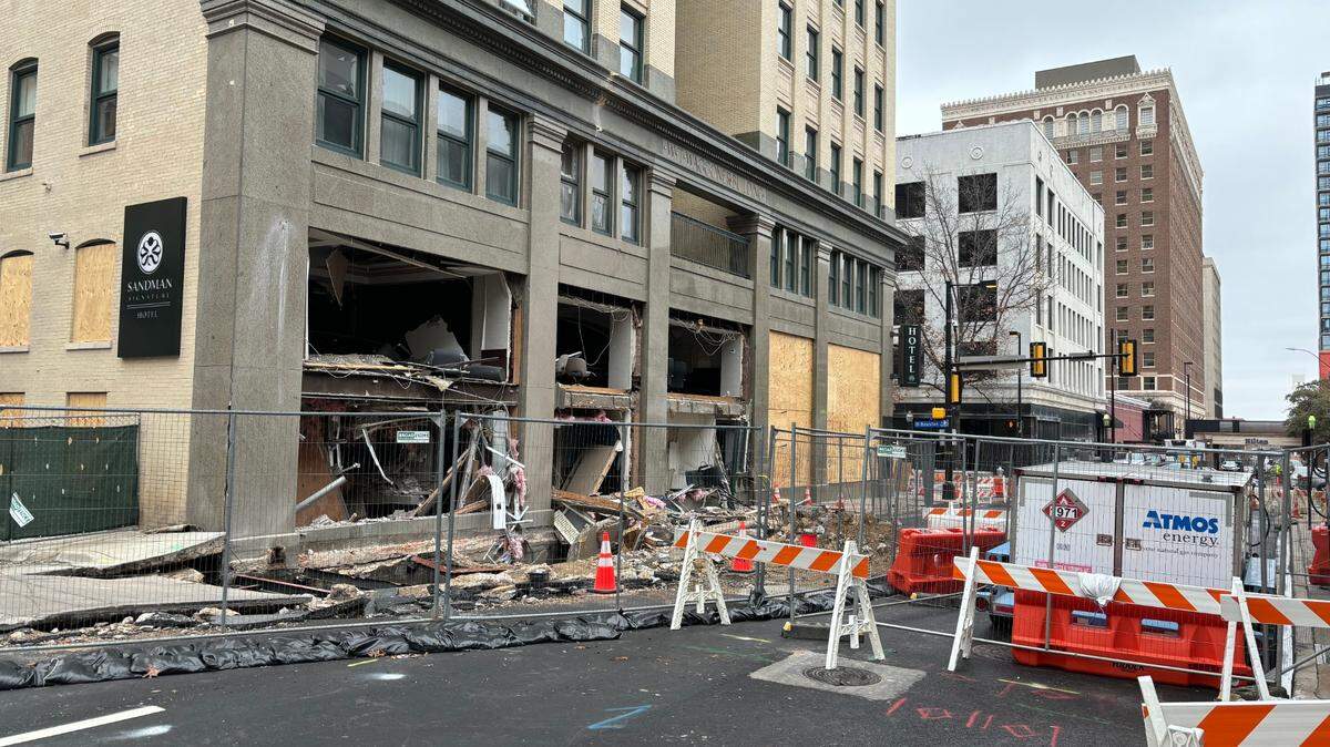 A downtown building with the ground floor windows blown out and debris on the street.